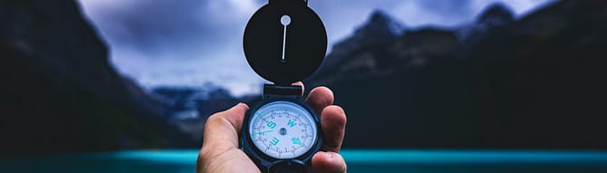 A hand holding a compass in front of a beautiful view